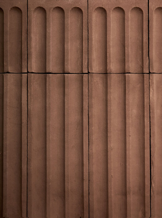 Rivestimento murale con piastrelle rettangolari in terracotta con rilievi verticali.