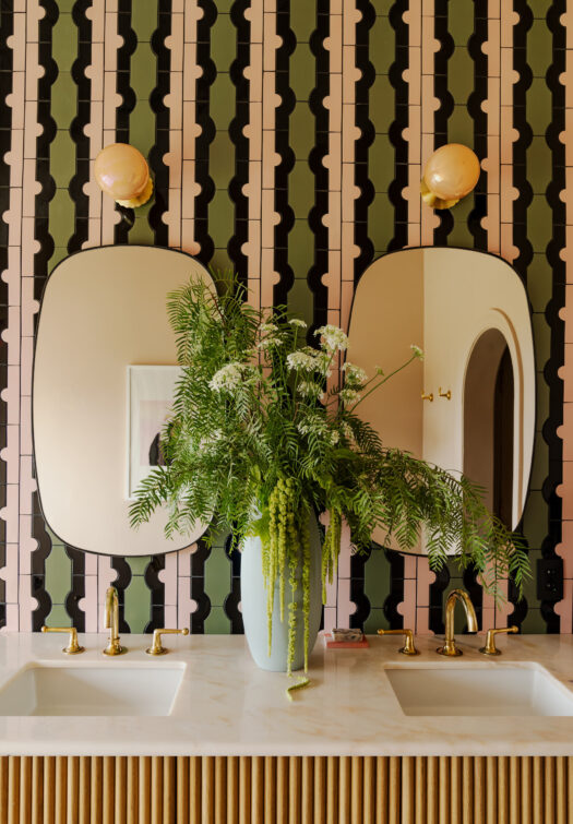 Bagno con due lavabi, specchi ovali e una parete rivestita con piastrelle verdi e rosa.